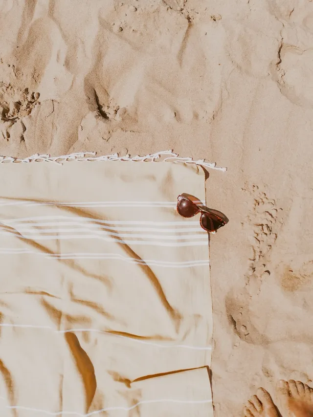 A beach towel and sunglasses on the sand